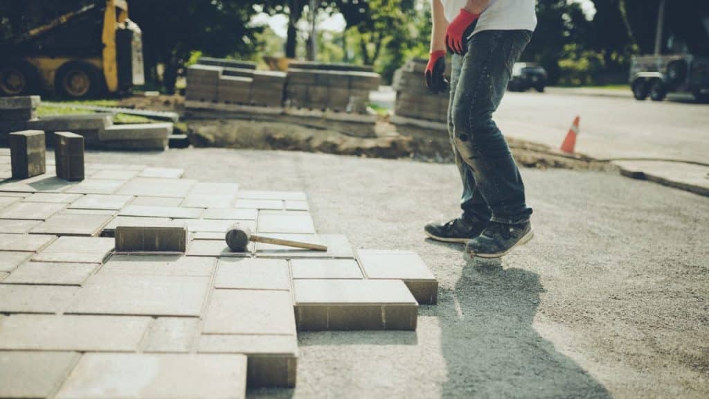 Worker installing pavers for driveway construction, showcasing process and tools used in creating durable and attractive outdoor surfaces