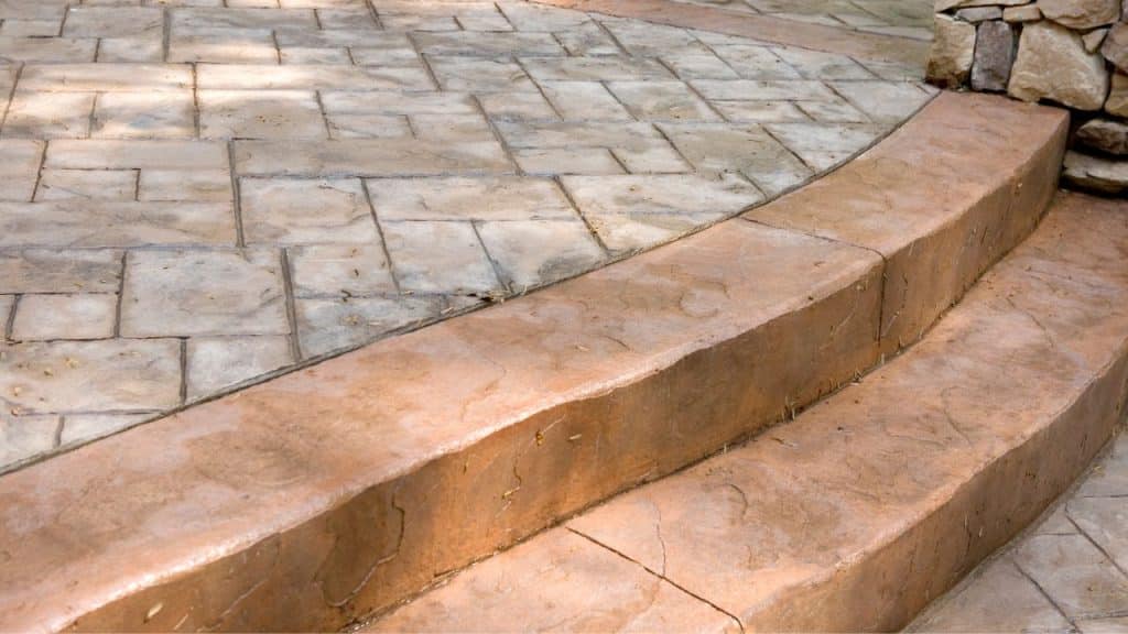 Stamped concrete patio with curved steps and stone wall border, showcasing intricate design and durability for outdoor spaces